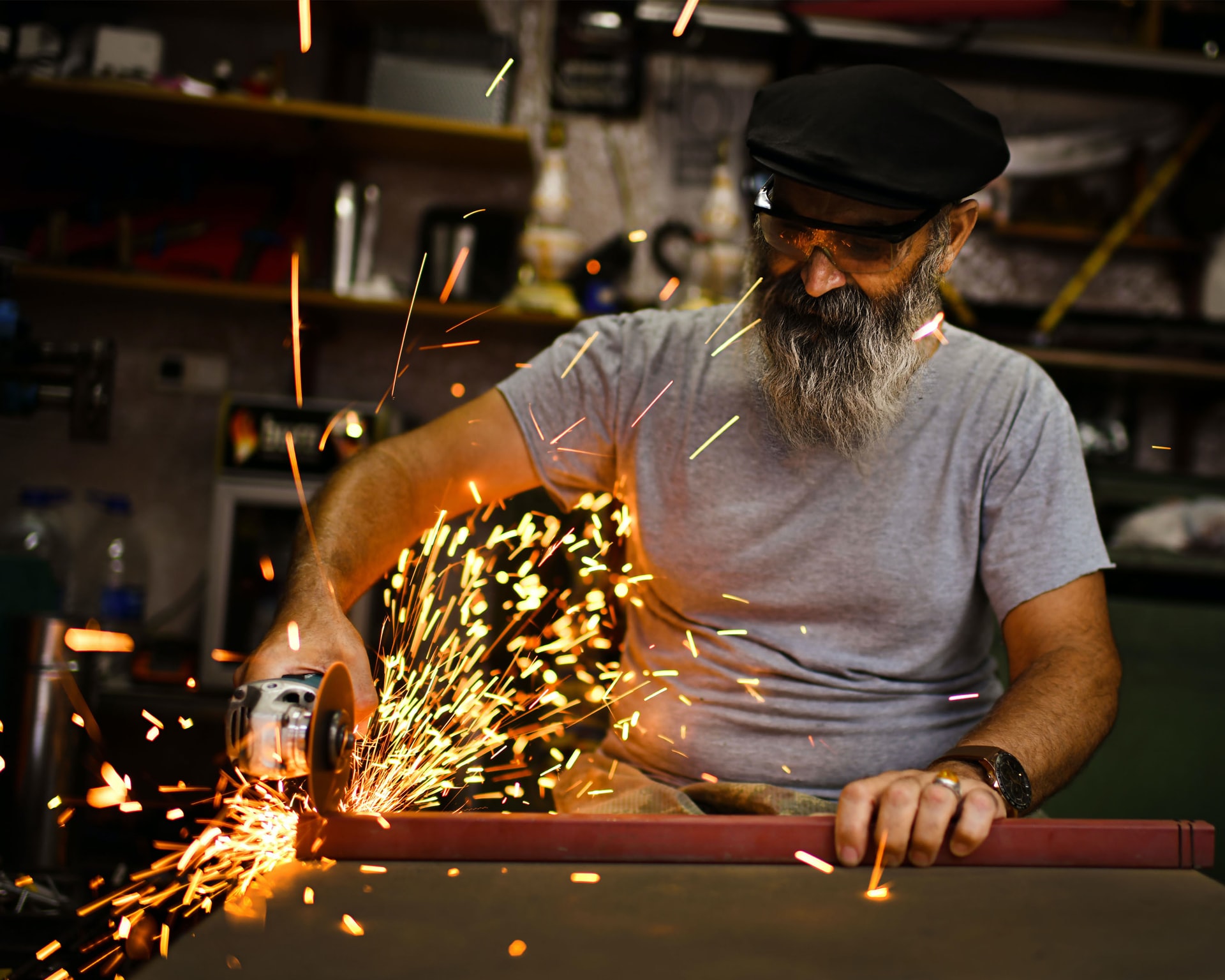 A grey bearded man using an angle grinder to cut metal. Sparks fly from the grinding wheel